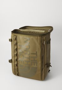 Olivgrön ryggsäck med en stor logotyp, dragkedjeöppning och sidostropper; tillverkad av ett hållbart, texturerat tyg med en strukturerad design.