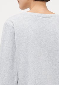 Grå bomullssweatshirt med en myk tekstur, med bred hals og senkede skuldre, vist fra baksiden, med fokus på stoffets utseende.
