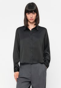 Camisa preta de cetim com botões e colarinho texturizado, mangas longas e um corte solto. Apresenta botões pretos na parte da frente.