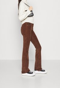 Bruna kordfløyelsbyxor med utsvängd nederdel och strukturerad yta, bärs med en vit tröja och svart handväska. Stylat med vita sneakers.