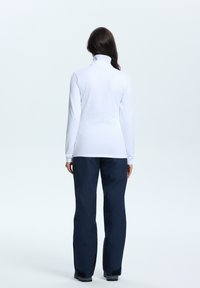 Biała bluzka z długim rękawem i wysokim kołnierzem, w połączeniu z granatowymi wodoodpornymi spodniami o luźnym kroju i czarnymi akcentami przy mankietach.