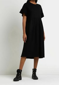 Svart, knälång klänning med korta volangärmar och en figurnära livdel, i kombination med svarta snörade ankelboots med metalliska detaljer.