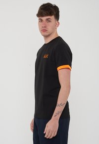 T-shirt nera a maniche corte con polsini arancioni e logo. Realizzata in cotone, presenta un collo rotondo e un design aderente.