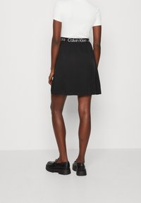 Černá sukně s elastickým pasem zdobeným bílým logem "Calvin Klein Jeans". Hladká látka, rozšířený střih, délka ke kolenům. Černé boty s robustní podrážkou.