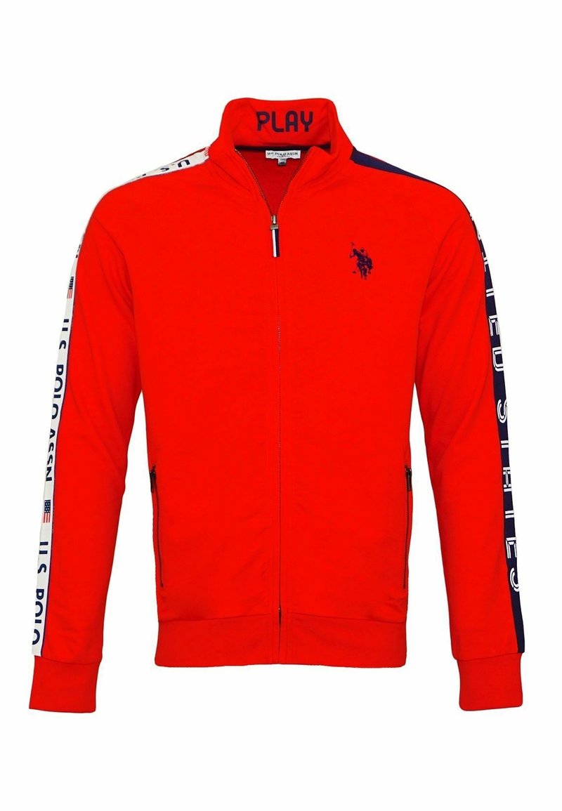 Veste de survêtement rouge zippée avec un logo bleu marine sur la poitrine, texte « "PLAY" » sur le col, et des bandes blanches avec le texte « "U.S. POLO ASSN." » le long des manches.