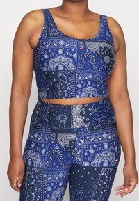 Torso of a person wearing a blue patchwork bandana-print crop top and matching high-waisted leggings.