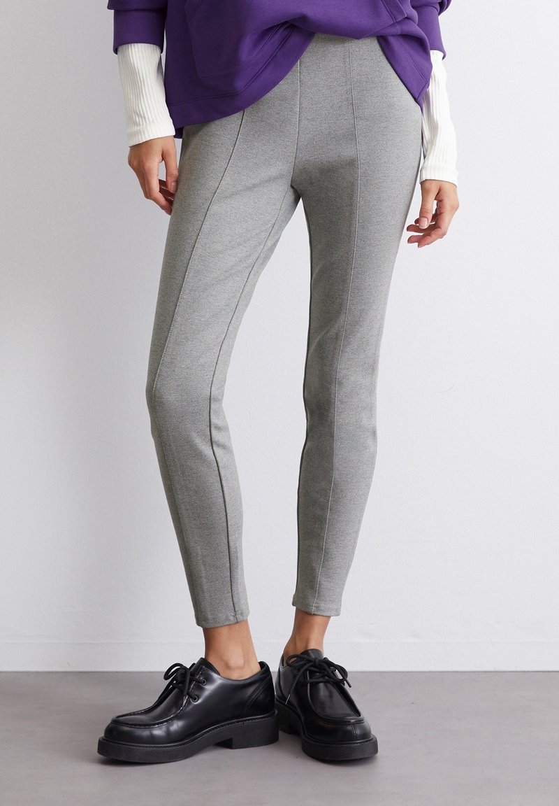 Leggings grigi aderenti realizzati in un tessuto morbido e elastico. Presentano una texture liscia con dettagli a cucitura verticale, abbinati a scarpe nere con lacci.