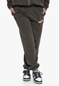 Dunkelgraue Jogginghose mit elastischem Bund, Seitentaschen und pinkem Grafiklogo. Kombiniert mit schwarz-weißen High-Top-Sneakern.