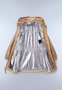 Tan outer jacket with a shiny silver lining. Features elastic cuffs, drawstrings, and a tag. Smooth texture throughout.