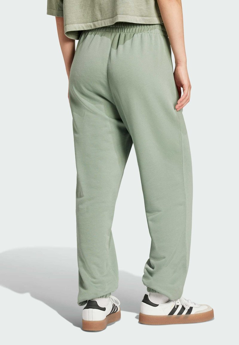 Light green joggers with an elastic waistband, cuffed ankle, and soft fabric, paired with white shoes featuring black stripes.