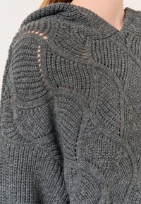 Poncho grigio lavorato a maglia con un motivo a onde testurizzato e un cappuccio, caratterizzato da dettagli a punto aperto per una maggiore traspirabilità e stile.