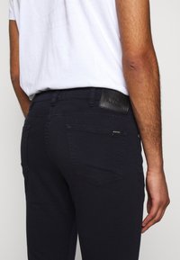 Mörkblå jeans gjorda av denim, med rakt snitt, design med fem fickor och ett svart lädermärke i midjan med präglad logotyp.