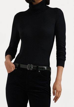 Personne portant un pull à col roulé noir à manches longues, un pantalon noir et une ceinture noire avec une boucle carrée argentée.