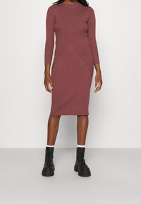 Ribbad midiklänning i dammig rosenfärg med långa ärmar och rundad halsringning. Har en figurnära silhuett och geometrisk texturdesign. Matchad med svarta kängor.