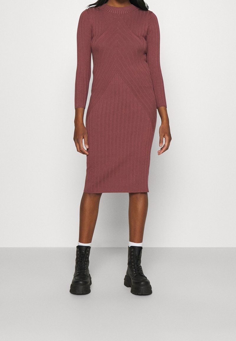 Ribbad midiklänning i dammig rosenfärg med långa ärmar och rundad halsringning. Har en figurnära silhuett och geometrisk texturdesign. Matchad med svarta kängor.