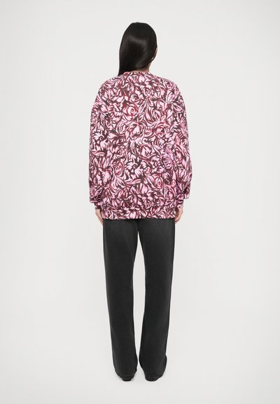 Chaqueta de estampado floral en rosa y negro con puños fruncidos, combinada con pantalones oscuros y holgados. El modelo se ve desde atrás.