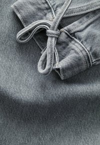 Hellgrauer Denim-Stoff mit einem gebundenen Kordelzugdetail. Die Textur ist weich mit einem leicht gerippten Muster und sichtbaren Nähten.