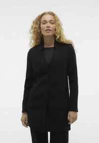 Blazer nero con colletto a revers, tasche frontali e maniche lunghe. Realizzato in un tessuto testurizzato con un design su misura.