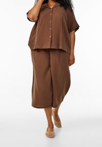 Braunes, strukturiertes, kurzärmliges Hemd mit Knopfleiste, kombiniert mit weit geschnittenen Culottes. Dazu werden leichte, gewebte Slipper mit entspannter Passform getragen.