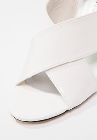 Sandale blanche à bout ouvert avec des larges brides entrecroisées et une finition lisse et brillante sur un fond blanc uni.