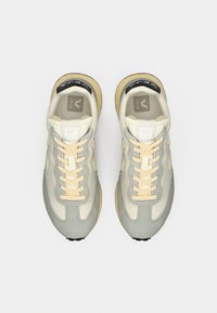 Ανοιχτό γκρι και κρεμ αθλητικά παπούτσια με λείες και σουέτ υφές, με κρεμ κορδόνια, λογότυπο στη γλώσσα και μαύρη λεπτομέρεια στη σόλα.