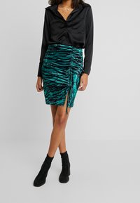 Svart satin skjorta med knappar och en teal och svart randig rynkad kjol med sidospalt. Bärs med svarta ankelstövlar.