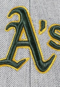 Graue Baseballmütze mit gesticktem "A's"-Schriftzug in Grün und Gelb, detaillierter Nähte und einem strukturierten Stoffhintergrund.
