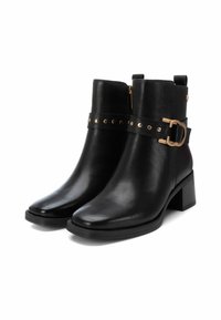 Botas de cuero negras hasta el tobillo con cremallera lateral, tacón grueso, acentos de herrajes dorados y una correa con tachuelas y detalle de hebilla.