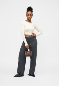 Εκρού cropped μπλούζα με μακριά μανίκια, γκρι ψηλόμεσα παντελόνια, μαύρα μυτερά παπούτσια και μια μικρή καφέ τσάντα χειρός. Λείες υφές και ραμμένη εφαρμογή.