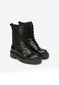 Černé boty s kombinací hladké kůže a prošívané látky. Mají robustní podrážku, šněrování a dva úchyty pro snadné obouvání.