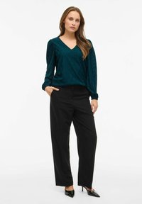 Teal-gepatrooneerde top met een V-hals en puffmouwen, gecombineerd met zwarte wijde broekspijpen en zwarte puntige hakken. Eenvoudig en modern ontwerp.