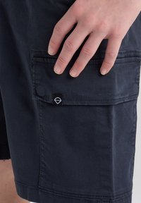 Pantaloni cargo blu con tessuto in cotone morbido, caratterizzati da una tasca laterale con patta e un piccolo etichetta marchiata.