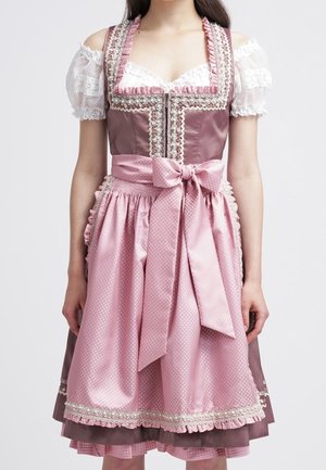 Frau trägt traditionelles Dirndl in Pink und Mauve mit spitzenbesetztem Mieder, gepufften Spitzenärmeln und einer großen Schleife, die am Taillenschurz gebunden ist.