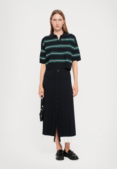 Marineblauwe geribde polo met meerkleurige strepen, gecombineerd met een hooggewaaid, knoopsluiting, geplooide rok en zwarte instappers. Handtas inbegrepen.