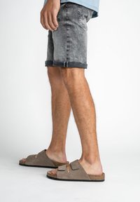 Bruna mockaskinn-slide sandaler med två remmar, korksulor och en texturerad yta; tillsammans med grå denimshorts med uppvikta kantar.