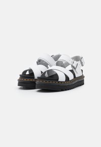 Weiße Ledersandalen mit verstellbaren Riemen, schwarzer Gummisohle und orangefarbenen Nähten. Offene Zehenpartie mit strukturiertem Finish.