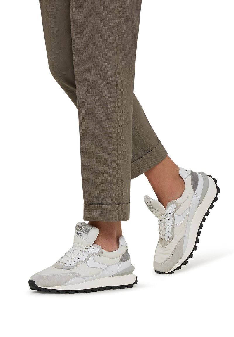 Sneakers bianchi e grigio chiaro con una combinazione di materiali in rete e suede, caratterizzati da una suola in gomma nera e un design testurizzato sulla parte superiore.