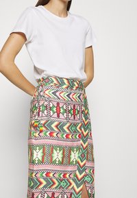 White cotton T-shirt paired with a multicolored patterned skirt, featuring geometric designs in pink, green, red, and yellow, with a side slit.