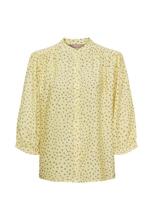 Lys gul bluse med brune polkaprikker, knaplukning foran, trekvart puffede ærmer og en lille stående krave.
