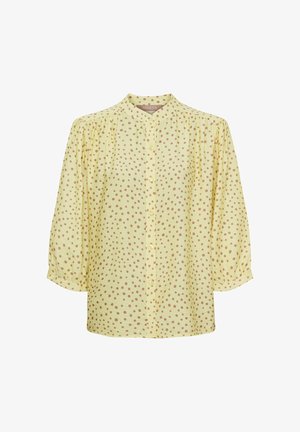 Lys gul bluse med brune polkaprikker, knaplukning foran, trekvart puffede ærmer og en lille stående krave.