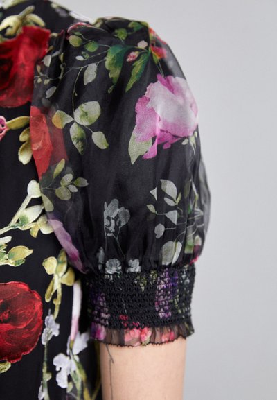 Floral blouse with black sheer fabric, featuring large red and pink roses. Puff sleeve details with ruched black elastic at the cuff.