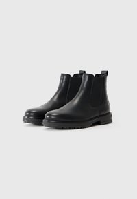Botas Chelsea de cuero negro con paneles laterales elásticos, puntera redondeada y suelas de goma texturizadas. Presenta tiradores para facilitar su puesta.