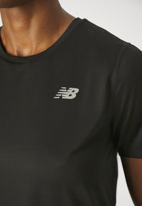Black athletic t-shirt with a round neckline, short sleeves, and a reflective New Balance logo on the chest. Textured fabric finish.