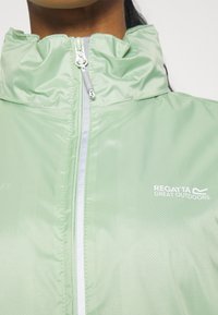 Gros plan d'une personne portant une veste vert clair Regatta Great Outdoors avec un col montant et une fermeture éclair à l'avant.