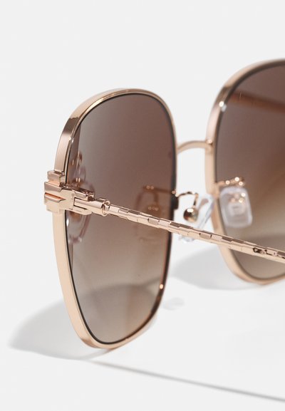 Occhiali da sole con tonalità marrone e montatura in metallo rosa oro, forma quadrata, stanghette texturizzate e naselli integrati per il comfort.