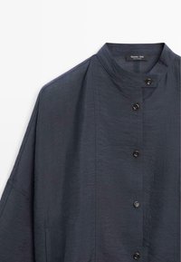 Mörk marinblå lätt skjorta med ståkrage och svarta knappar, visar övre vänstra framsidan och axeln.