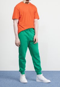 Oranžové bavlněné tričko, zelené tepláky a bílé tenisky. Tričko má kulatý výstřih, kalhoty mají elastický pas a manžety.