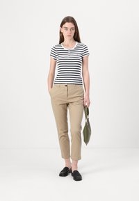 Ribade mustriline musta ja valge lühikeste varrukatega topp, nööbitav kaelus; beežid kitsad püksid; roheline käekott; mustad madalad kingad; minimalistlik disain.
