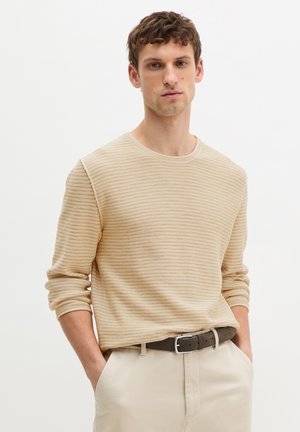 Beige sweater with horizontal stripes, round neckline, and long sleeves. Worn with light-colored trousers and a brown belt.