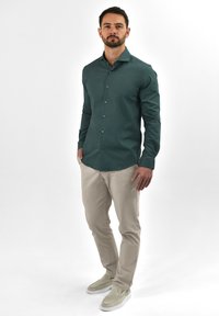 Donkergroen overhemd met knopen, heeft een slim fit, lange mouwen en een subtiele textuur. Gecombineerd met lichtbeige broek en instappers.